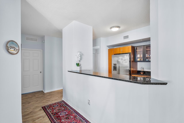 kitchen featuring dark stone counters, stainless steel fridge, a textured ceiling, light hardwood / wood-style floors, and kitchen peninsula