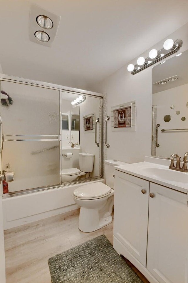 full bathroom with combined bath / shower with glass door, wood-type flooring, vanity, and toilet