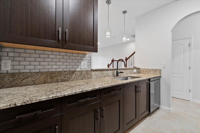 kitchen with sink, light stone counters, stainless steel dishwasher, backsplash, and decorative light fixtures