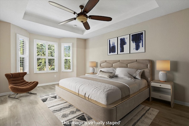 bedroom featuring ceiling fan, wood-type flooring, and a tray ceiling