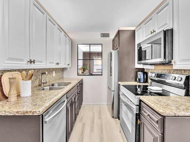 kitchen featuring sink, decorative backsplash, light hardwood / wood-style floors, stainless steel appliances, and light stone countertops