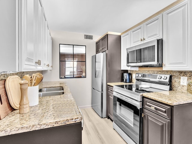 kitchen with tasteful backsplash, white cabinetry, sink, stainless steel appliances, and light wood-type flooring