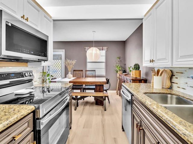 kitchen featuring a sink, backsplash, white cabinetry, light wood-style floors, and appliances with stainless steel finishes