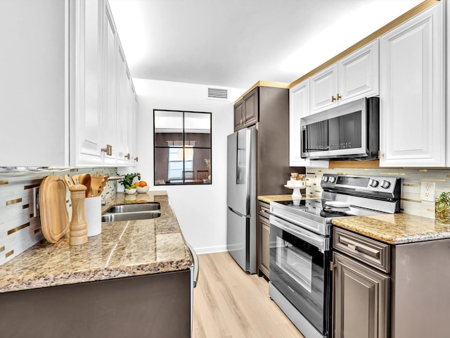 kitchen featuring visible vents, light wood-style flooring, a sink, appliances with stainless steel finishes, and tasteful backsplash