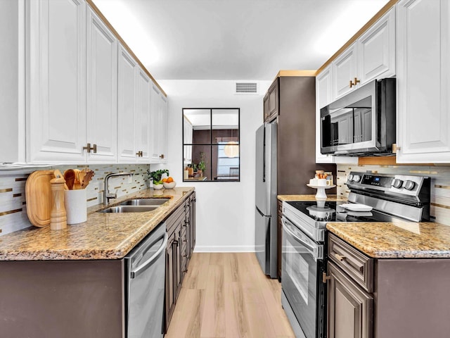 kitchen featuring visible vents, a sink, decorative backsplash, stainless steel appliances, and light wood-type flooring