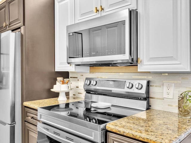 kitchen featuring tasteful backsplash, white cabinets, appliances with stainless steel finishes, and light stone counters