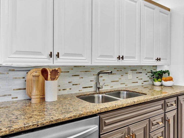 kitchen featuring light stone countertops, white cabinetry, a sink, stainless steel dishwasher, and tasteful backsplash