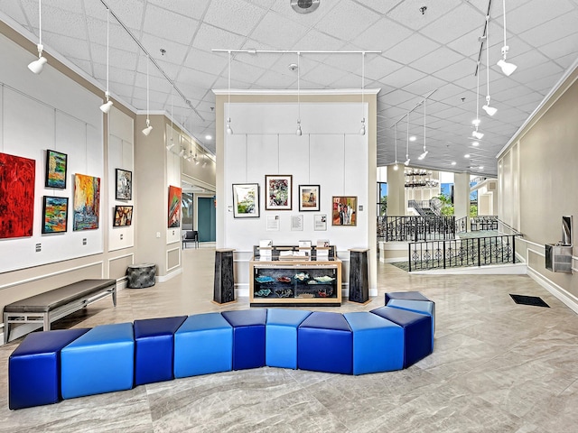 living room with a drop ceiling, a high ceiling, crown molding, and baseboards