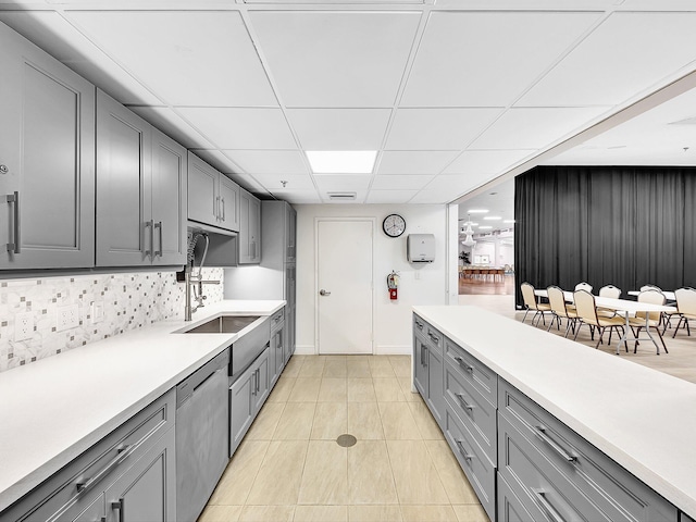 kitchen with a drop ceiling, dishwasher, light countertops, light tile patterned floors, and gray cabinets