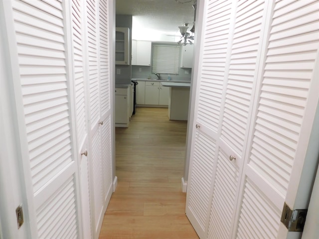 corridor with a textured ceiling, light wood-type flooring, and sink