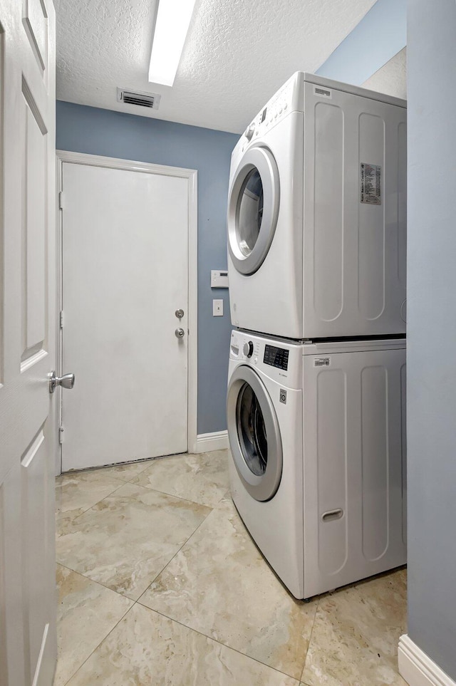 clothes washing area featuring a textured ceiling and stacked washer / dryer