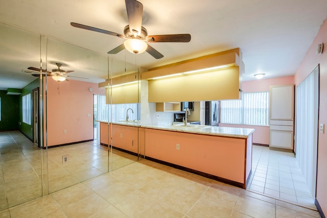 kitchen featuring kitchen peninsula, stainless steel fridge, ceiling fan, sink, and light tile patterned floors