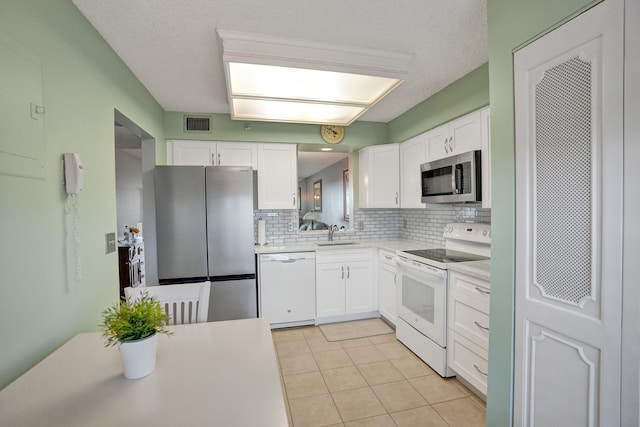 kitchen with white cabinetry, stainless steel appliances, a textured ceiling, decorative backsplash, and light tile patterned floors