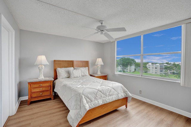 bedroom with a textured ceiling, light wood-type flooring, and ceiling fan