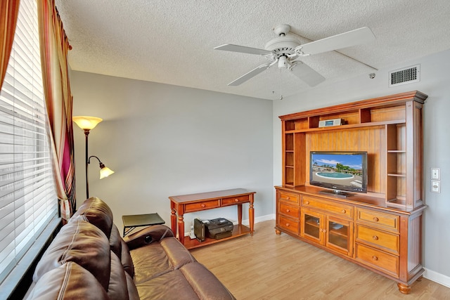 living room featuring ceiling fan, light hardwood / wood-style floors, and a textured ceiling