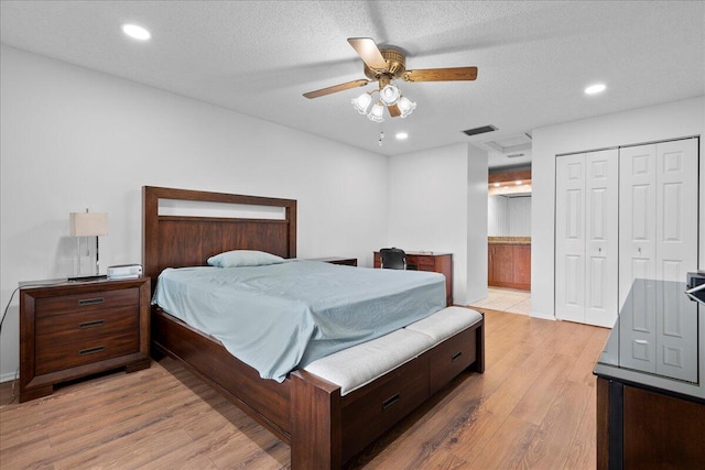 bedroom featuring ceiling fan, a textured ceiling, connected bathroom, light hardwood / wood-style floors, and a closet