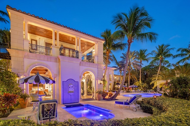 rear view of property featuring a swimming pool with hot tub, a balcony, and a patio area