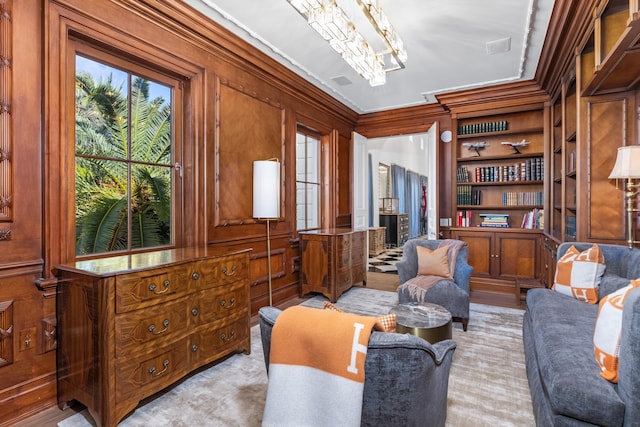 sitting room featuring built in shelves, a wealth of natural light, wooden walls, and ornamental molding