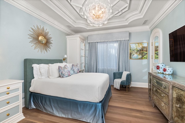 bedroom featuring a raised ceiling, ornamental molding, a notable chandelier, and hardwood / wood-style flooring