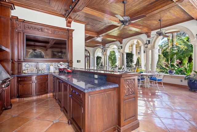 kitchen with wooden ceiling, dark stone counters, sink, kitchen peninsula, and decorative columns