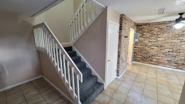 stairway with tile patterned floors, ceiling fan, a textured ceiling, and brick wall