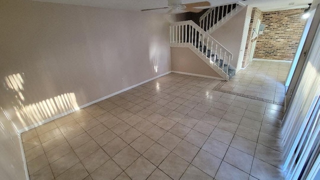 tiled spare room with ceiling fan and brick wall