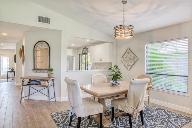 dining area with light hardwood / wood-style flooring, vaulted ceiling, and an inviting chandelier