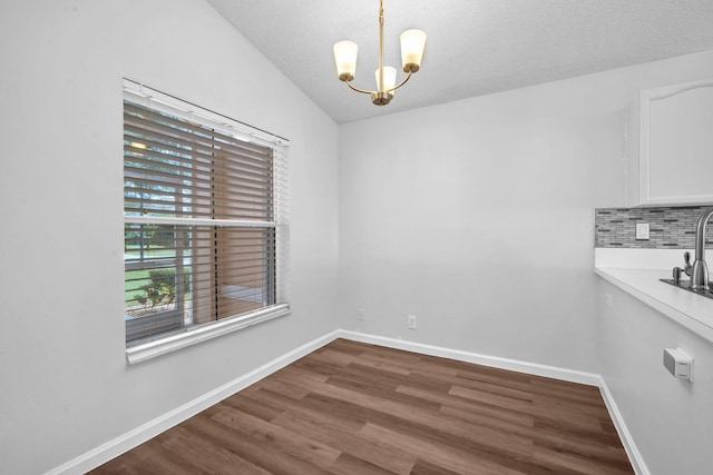 unfurnished dining area with hardwood / wood-style floors, an inviting chandelier, sink, vaulted ceiling, and a textured ceiling