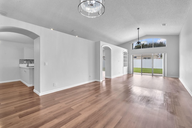 unfurnished living room with ceiling fan with notable chandelier, wood-type flooring, a textured ceiling, and vaulted ceiling