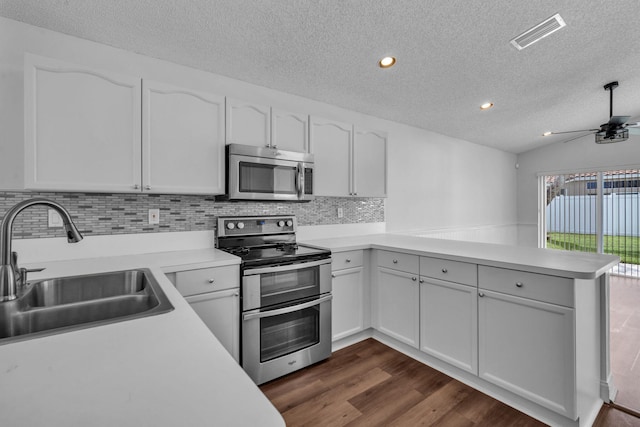 kitchen with kitchen peninsula, stainless steel appliances, vaulted ceiling, sink, and white cabinetry