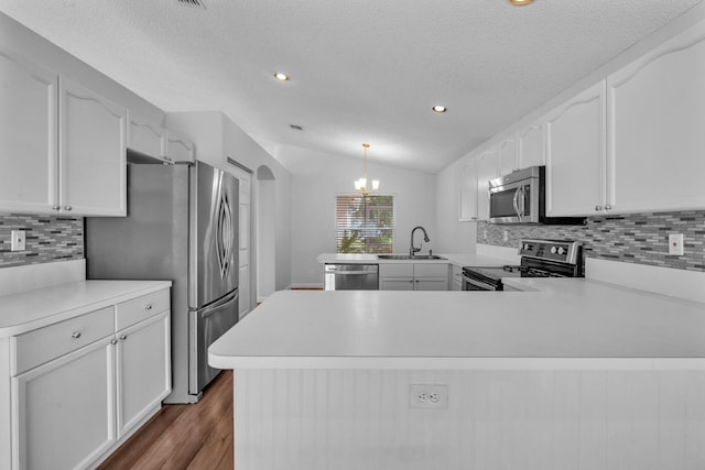 kitchen featuring pendant lighting, lofted ceiling, sink, appliances with stainless steel finishes, and kitchen peninsula