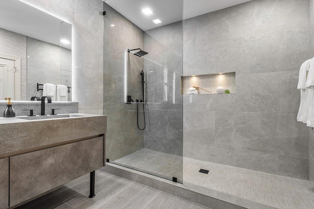 bathroom with vanity, tiled shower, and tile walls