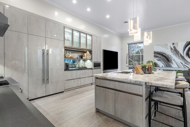 kitchen with a kitchen bar, light stone counters, crown molding, sink, and decorative light fixtures