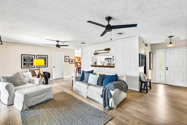 living room with ceiling fan, a textured ceiling, and light hardwood / wood-style flooring