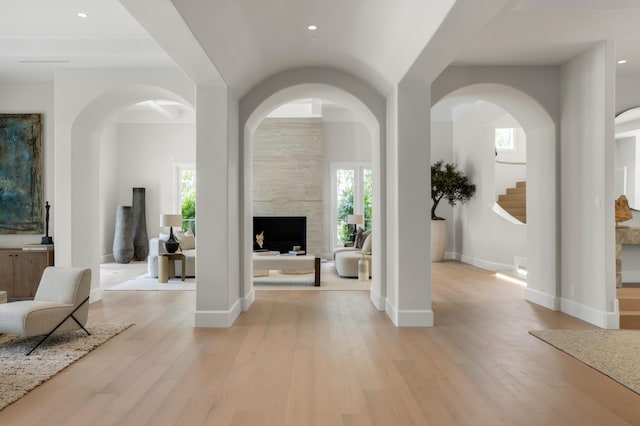 foyer featuring light wood-type flooring, a large fireplace, baseboards, and stairs