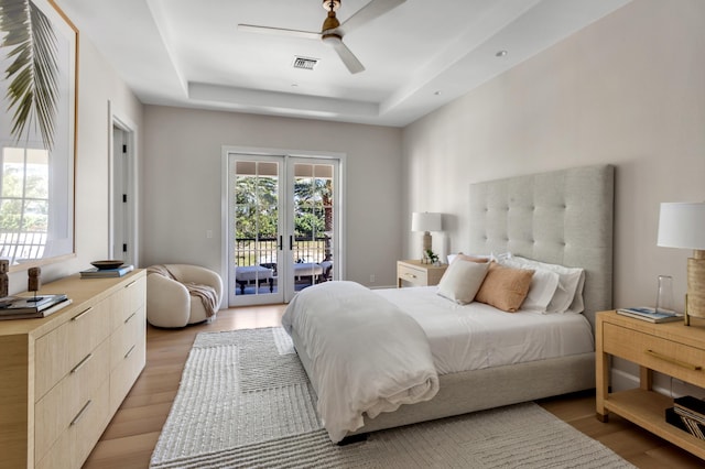 bedroom with access to exterior, visible vents, a tray ceiling, light wood-style flooring, and french doors