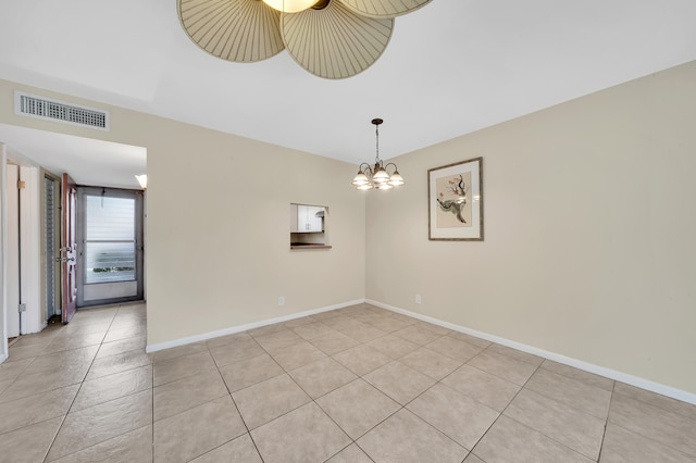 empty room with light tile patterned floors and an inviting chandelier