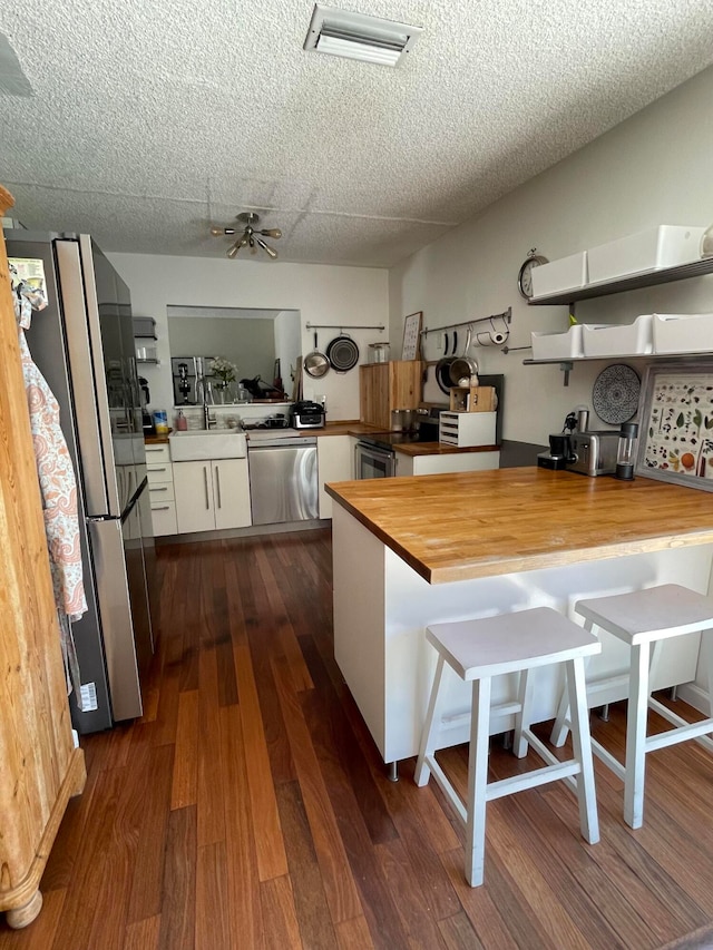 kitchen featuring wood counters, white cabinets, appliances with stainless steel finishes, dark hardwood / wood-style flooring, and a breakfast bar area