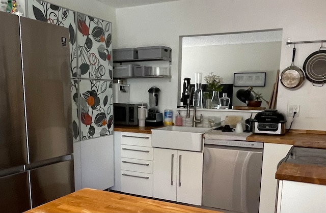 kitchen with wood counters, appliances with stainless steel finishes, white cabinetry, and sink