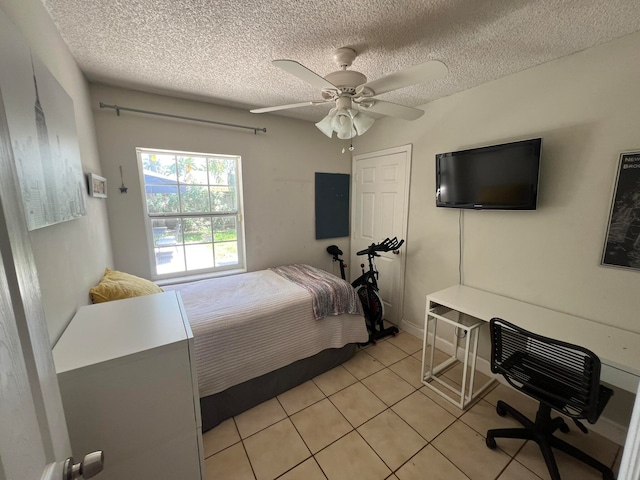 bedroom featuring ceiling fan, light tile patterned floors, and a textured ceiling