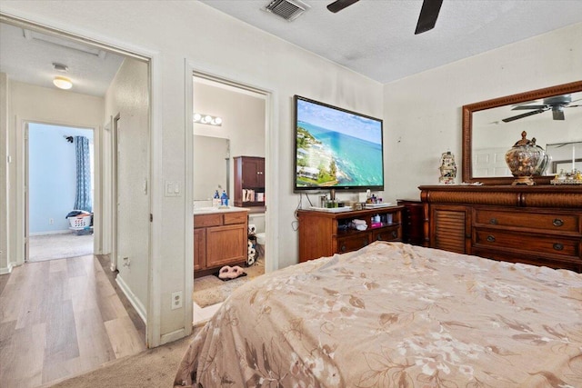 bedroom with ensuite bathroom, ceiling fan, a textured ceiling, and light hardwood / wood-style flooring