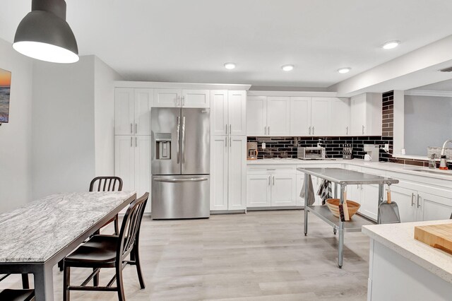 kitchen with hanging light fixtures, white cabinets, stainless steel appliances, and light hardwood / wood-style flooring