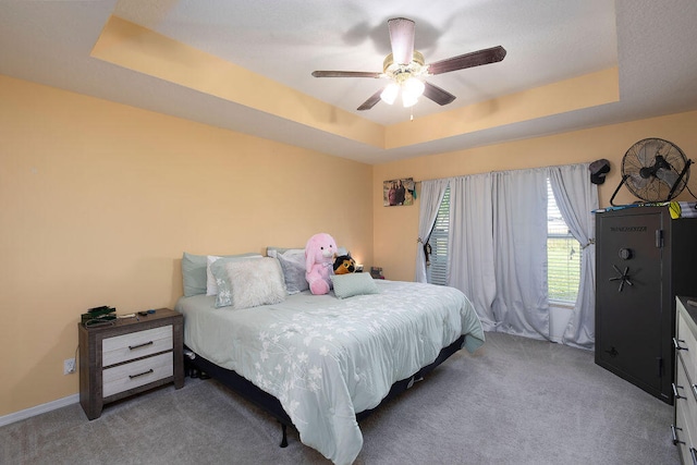 carpeted bedroom with a raised ceiling and ceiling fan