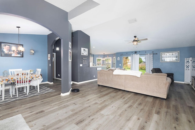 living room featuring ceiling fan with notable chandelier, vaulted ceiling, and wood-type flooring