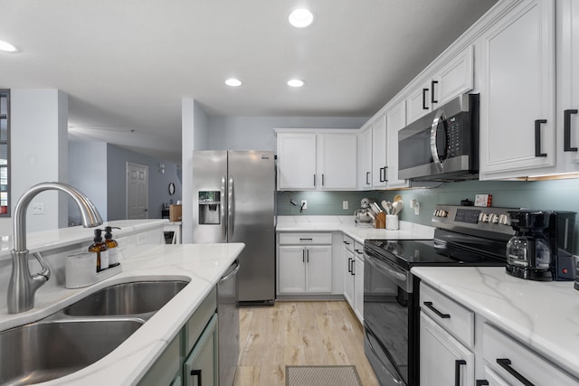 kitchen with appliances with stainless steel finishes, light wood-type flooring, light stone counters, sink, and white cabinets