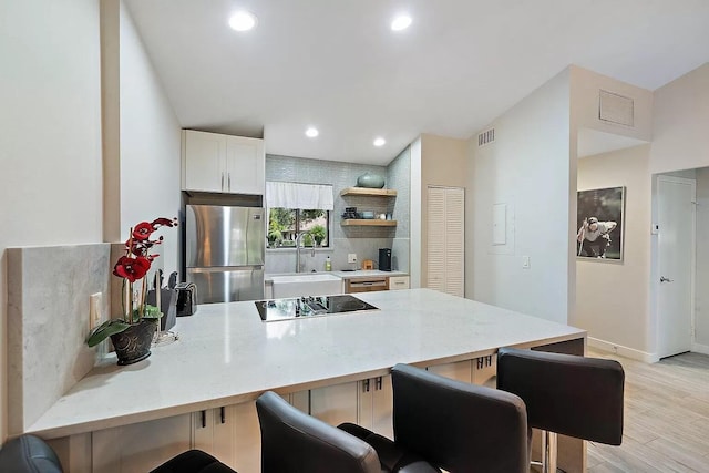 kitchen featuring sink, kitchen peninsula, light hardwood / wood-style floors, a breakfast bar, and appliances with stainless steel finishes