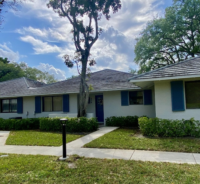 single story home featuring a front lawn, a tile roof, and stucco siding