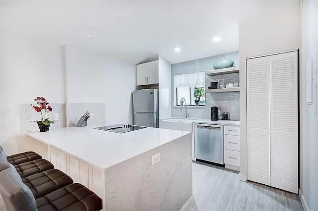 kitchen featuring a breakfast bar, light hardwood / wood-style flooring, white cabinetry, kitchen peninsula, and stainless steel appliances