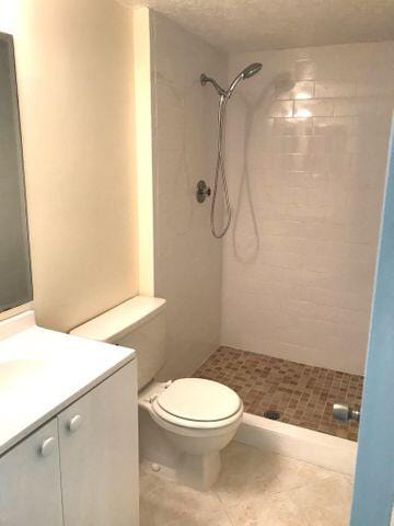 bathroom featuring tile patterned flooring, a textured ceiling, tiled shower, toilet, and vanity