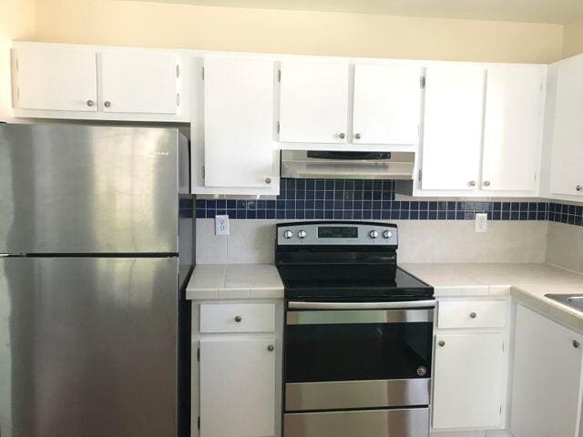 kitchen with appliances with stainless steel finishes, ventilation hood, white cabinetry, and tasteful backsplash